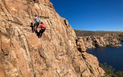 Two people on side of cliff with lake in background.