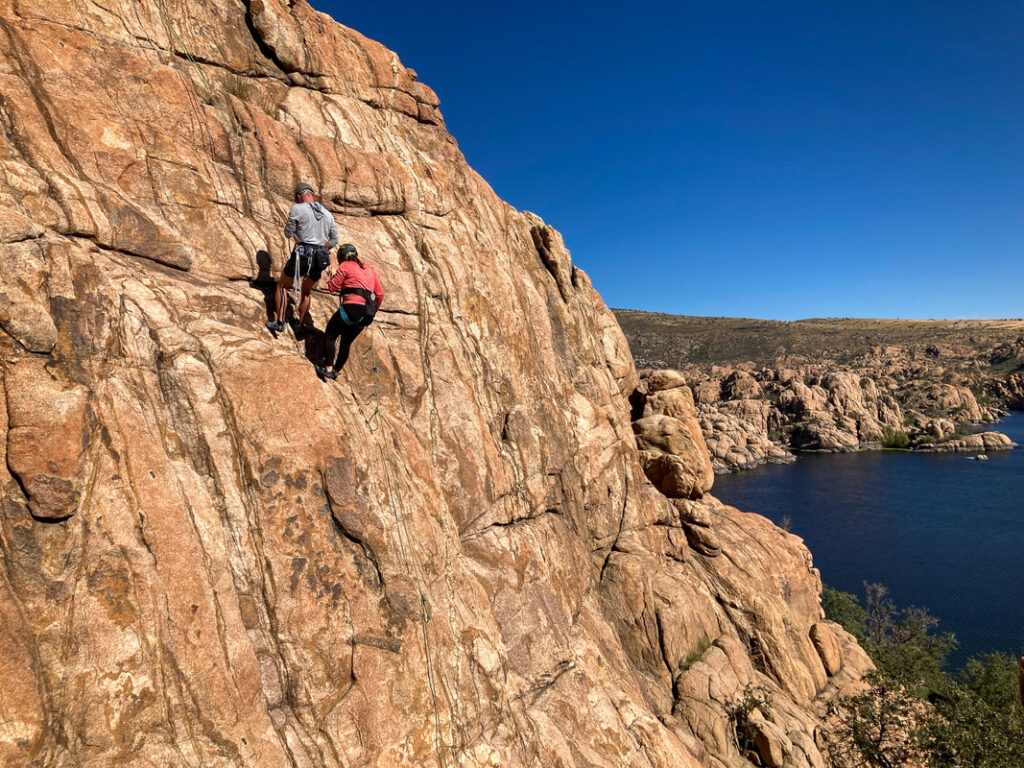 Two people on side of cliff with lake in background